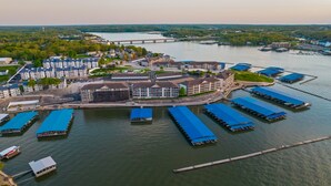 An aerial view of a waterfront hotel with multiple docked boats, a bridge in the background, and a forested landscape. - Breathtaking View - Top Floor Lands End Condo, POOL & lazy river! BEST location! (Osage Beach)
