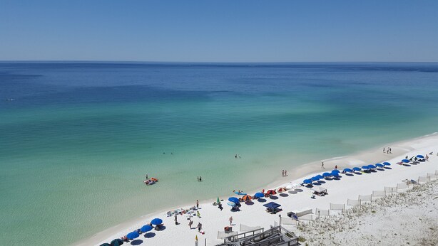 A beach with clear turquoise water, a sandy shore, and several umbrellas and beach chairs. - Amazing Beachfront Destin Condo With Ocean Views from All Rooms (Destin)