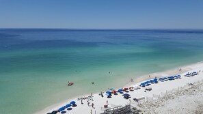 A beach with clear turquoise water, a sandy shore, and several umbrellas and beach chairs.
