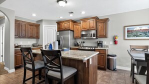 A kitchen with wooden cabinets, stainless steel appliances, granite countertops, and a central island with bar stools.