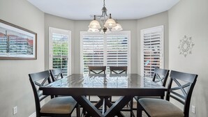A dining room with a glass-top table, black chairs, and a chandelier.