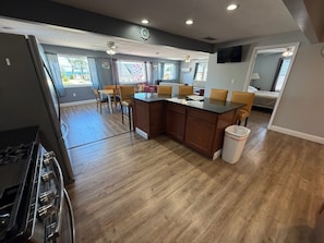 A modern kitchen with a central island, wooden flooring, and a dining area with chairs.