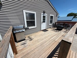 A wooden deck with a grill, a door, and a seating area with chairs and tables.
