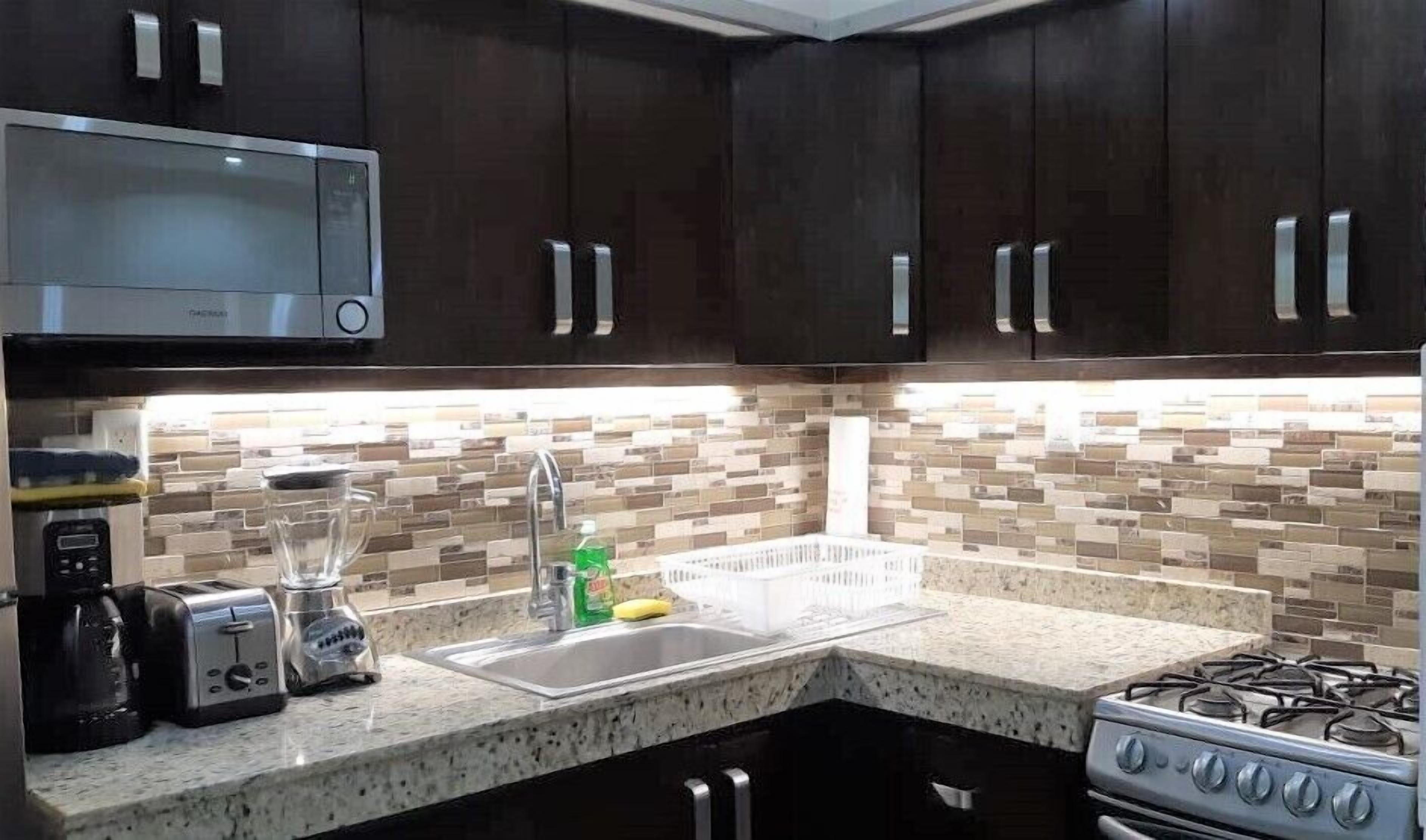 A kitchen with dark cabinets, a microwave, a toaster, a blender, a sink, and a stove.
