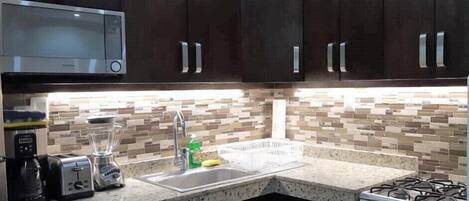 A kitchen with dark cabinets, a microwave, a toaster, a blender, a sink, and a stove.
