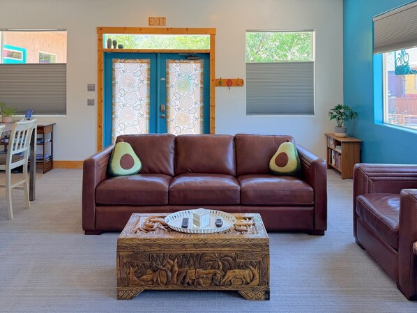 A living room with a brown leather sofa, a coffee table with carvings, and a door with a blue frame. - Romantic getaway/ Staycation/ Friend trip home base! 1 M to ZNP, Shuttle stop #5 (Springdale)