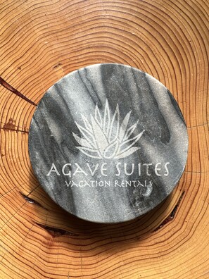 Pyöreä esine, jonka pinnassa on lehtikuviota ja teksti: ”AGAVE SUITES – LOMAMÖKKI VUOKRATTAVANA”.