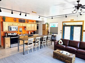 Una cocina moderna con armarios de madera, un comedor con mesa y sillas, un sofá de cuero marrón y un cofre decorativo de madera.