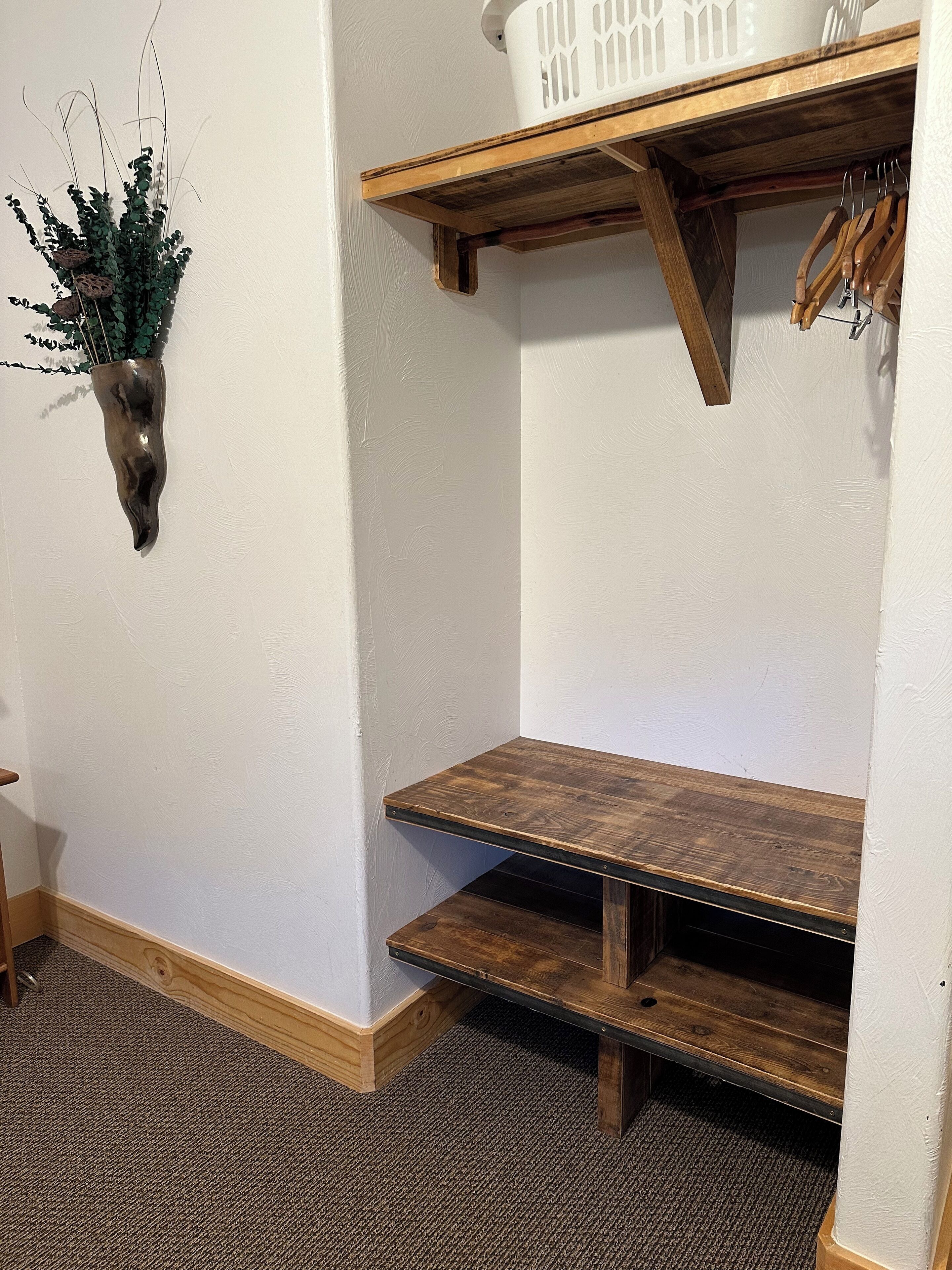 Eine Ecke mit einem Holzregal, einer hängenden Pflanzkorb und einer Holzbank.