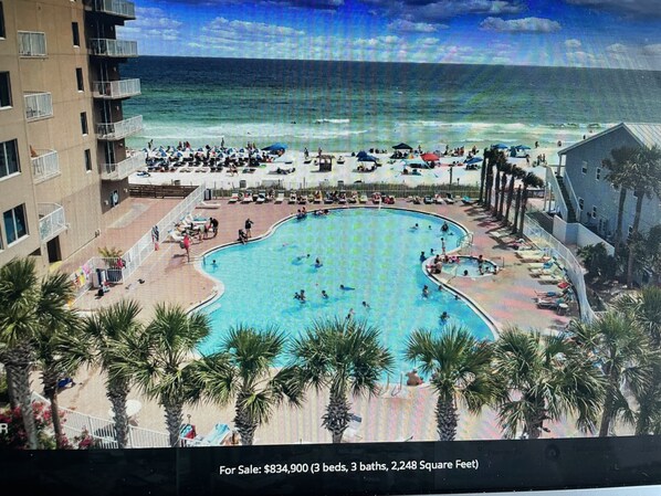 A large pool area with a view of the ocean, surrounded by palm trees and a building with balconies.