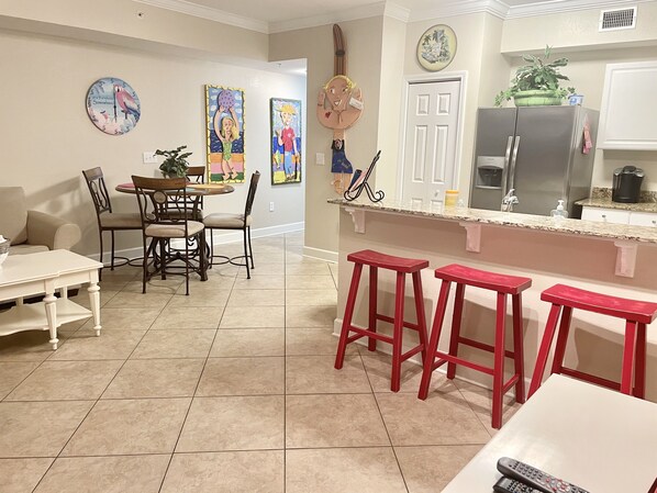 Una cocina moderna con una isla central, taburetes rojos y una zona de comedor con mesa y sillas.