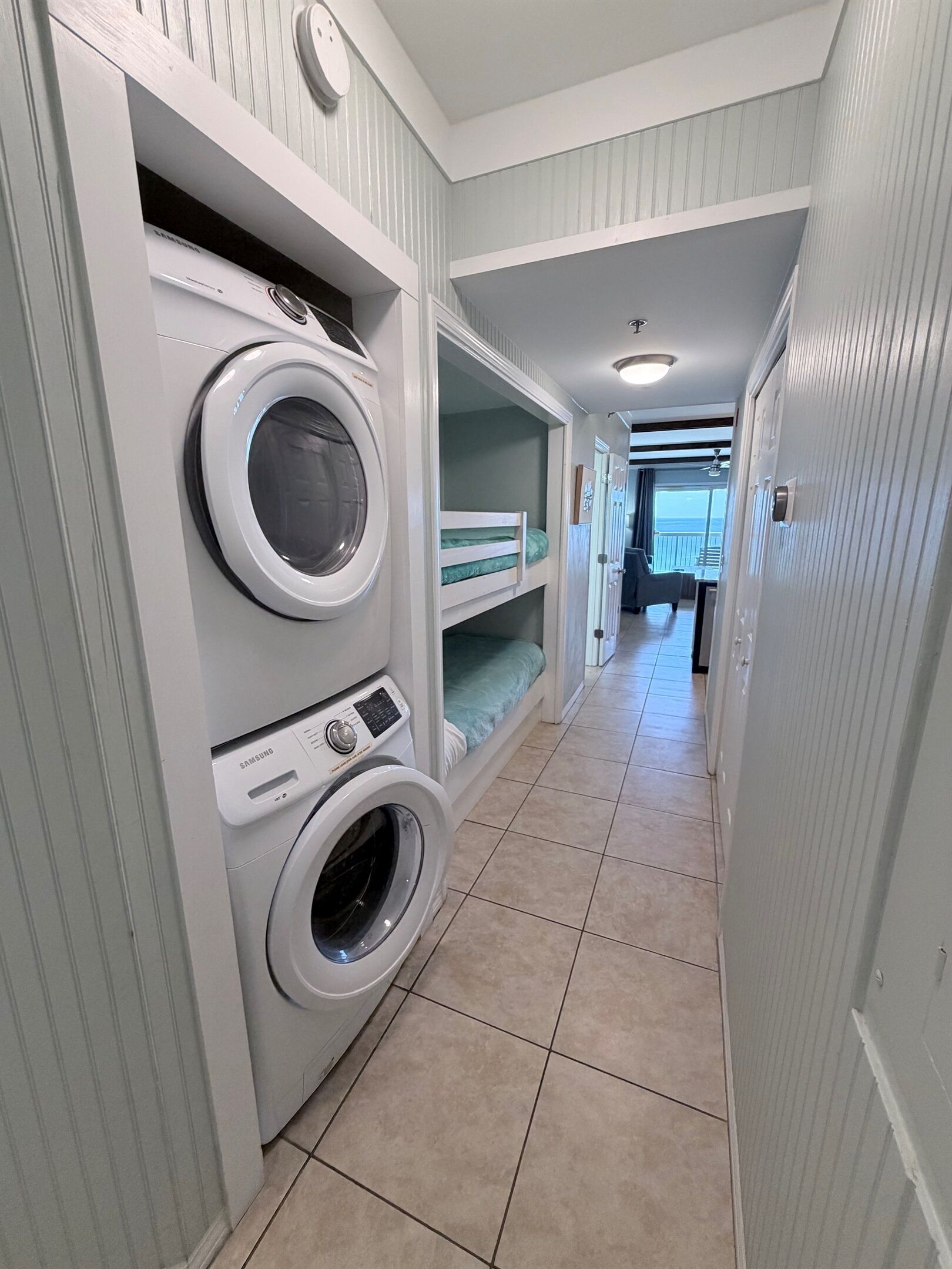A laundry room with two front-loading washers and dryers, a bunk bed, and a view of the ocean through a large window.
