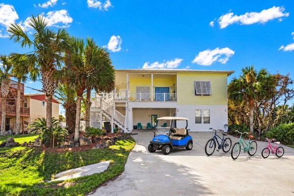 A two-story building with a balcony, a golf cart, and bicycles parked in front. - Seashell Paradise | Pool, Spa, Golf Cart, Bikes (Palm Coast)
