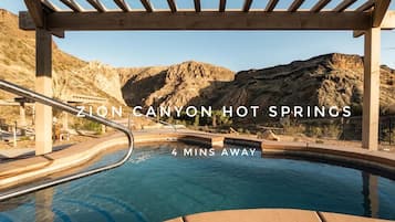 A hot spring pool with wooden pergolas and a mountainous backdrop.