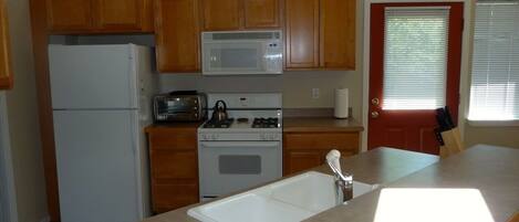 A kitchen with wooden cabinets, a white refrigerator, a microwave, a stove, and a sink.