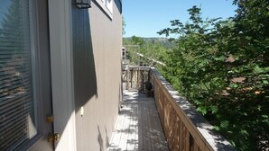 A wooden deck with a railing, a door with a window, and a view of trees and hills in the background. - Stay In The Heart Of Bend, Walk Everywhere!   (Bend)