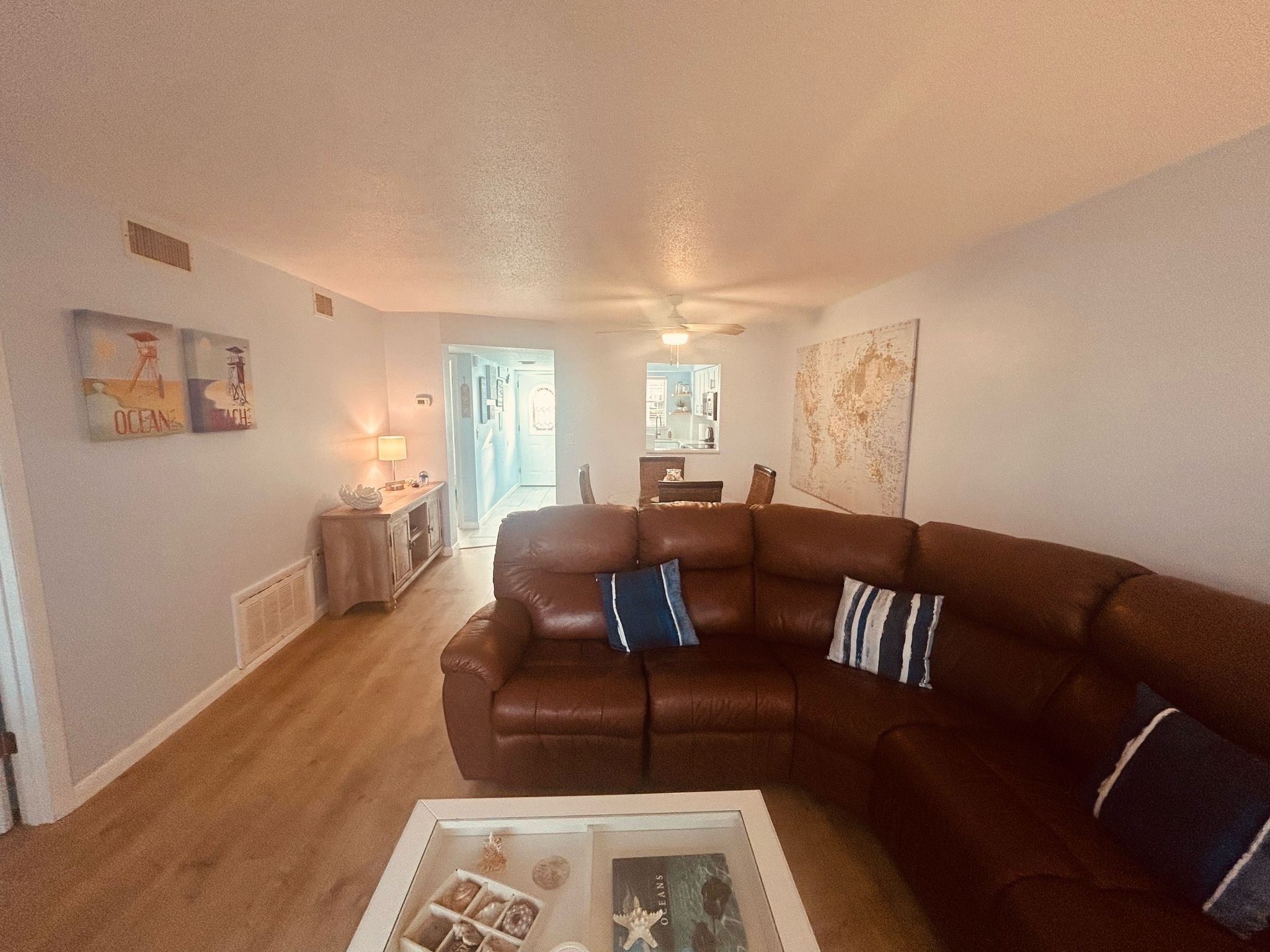 A living room with a brown leather sofa, a coffee table with decorative items, and a hallway leading to a kitchen.