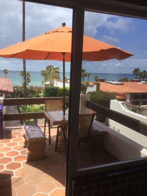 A balcony with a view of the ocean, featuring a table and chairs, an orange umbrella, and a tiled floor. - Ocean View - Unique Mexican Contemporary Vacation home with Amenities! (Las Gaviotas)