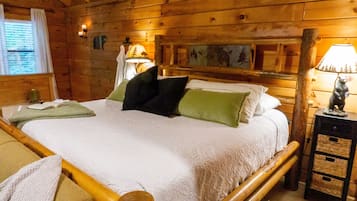 Een kamer in houten blokhutstijl met een bed, nachtkastje, lamp en een raam met gordijnen.