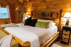 A wooden cabin-style room with a bed, a nightstand, a lamp, and a window with curtains. - Private Log Cabin with Hot Tub (Gatlinburg)