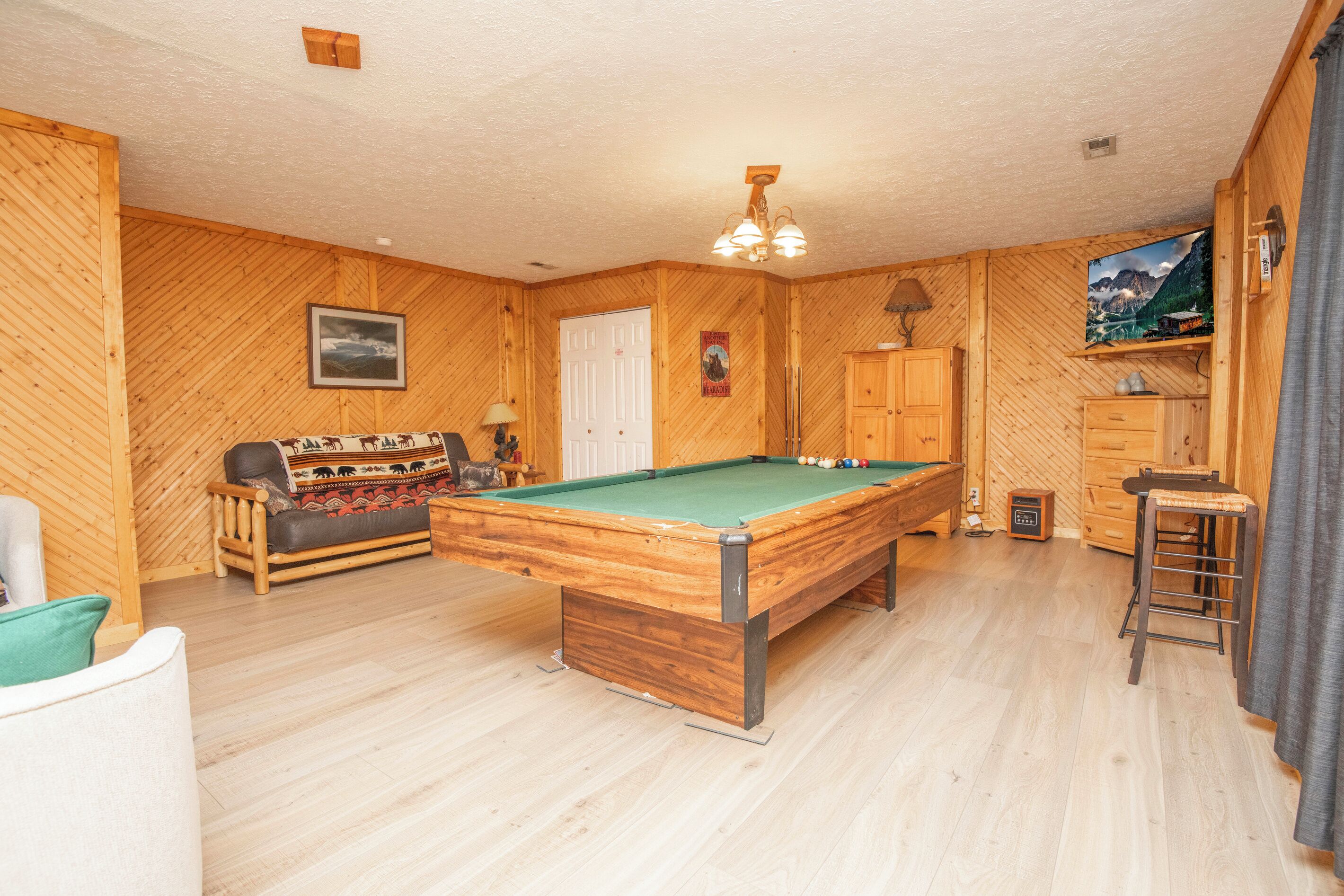 A wooden-floored room with a pool table, a sofa, and a cabinet.