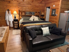 A log cabin interior with a bed, a leather sofa, a wooden dresser, a lamp, and a refrigerator. - Private Log Cabin with Hot Tub (Gatlinburg)