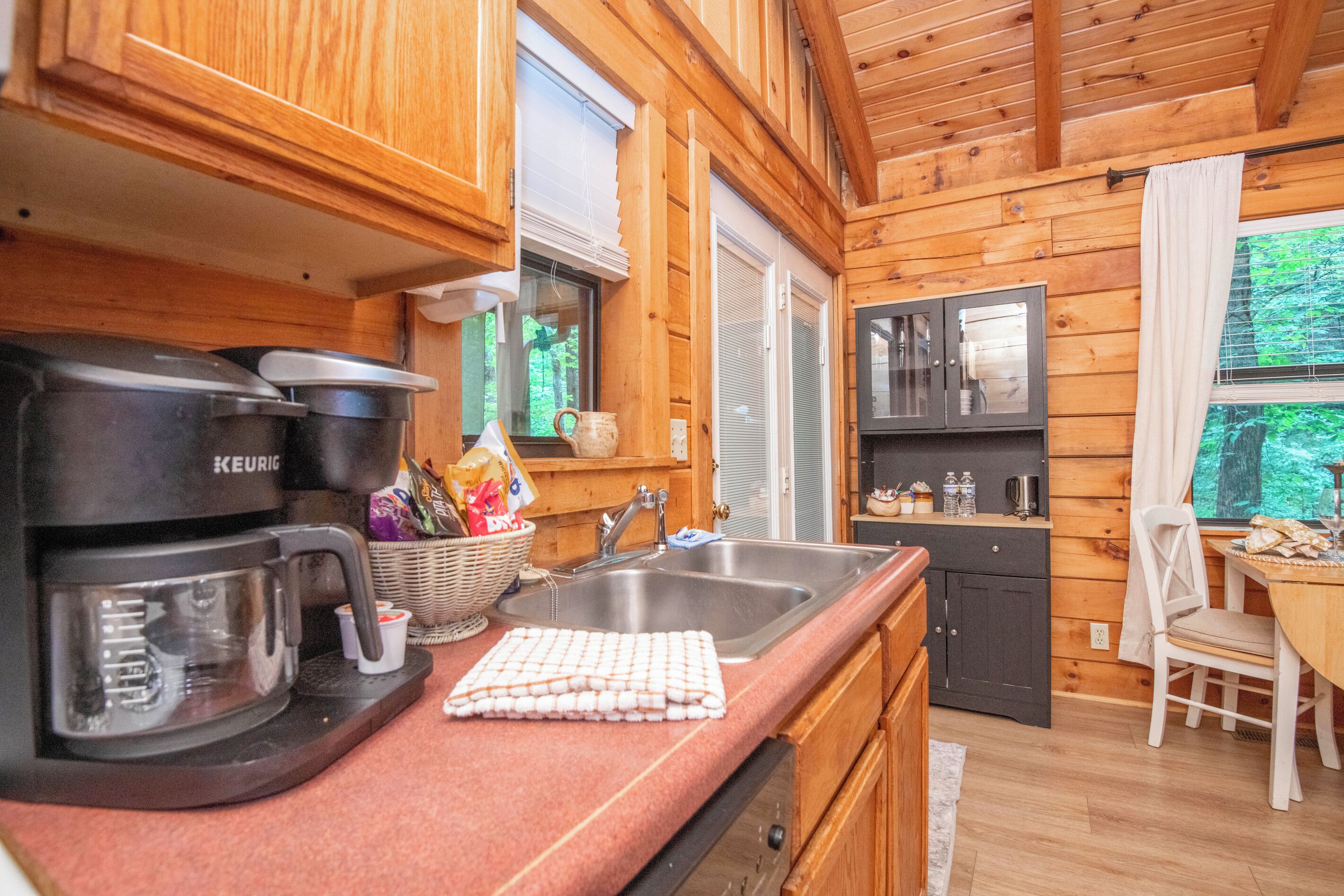 A wooden cabin interior with a kitchenette, a coffee maker, a sink, and a dining area.