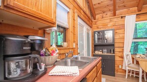 Interior de una cabaña de madera con kitchenette, cafetera, lavabo y comedor.