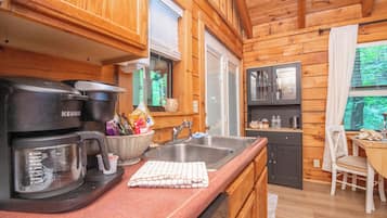 A wooden cabin interior with a kitchenette, a coffee maker, a sink, and a dining area.