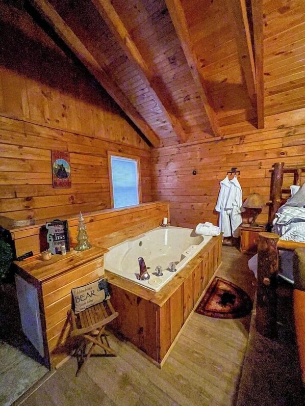 A wooden cabin interior with a large bathtub, a wooden bench, a small table, and a window. - Private Log Cabin with Hot Tub (Gatlinburg)