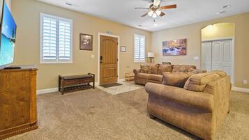 A living room with beige walls, a ceiling fan, a wooden door labeled "EXIT", a brown sofa, a wooden cabinet, and a television.