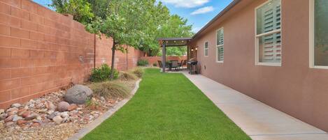 A patio area with a pergola, a barbecue setup, and a brick wall.