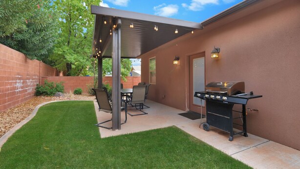 Un jardin avec un patio couvert, un barbecue et du mobilier d’extérieur.