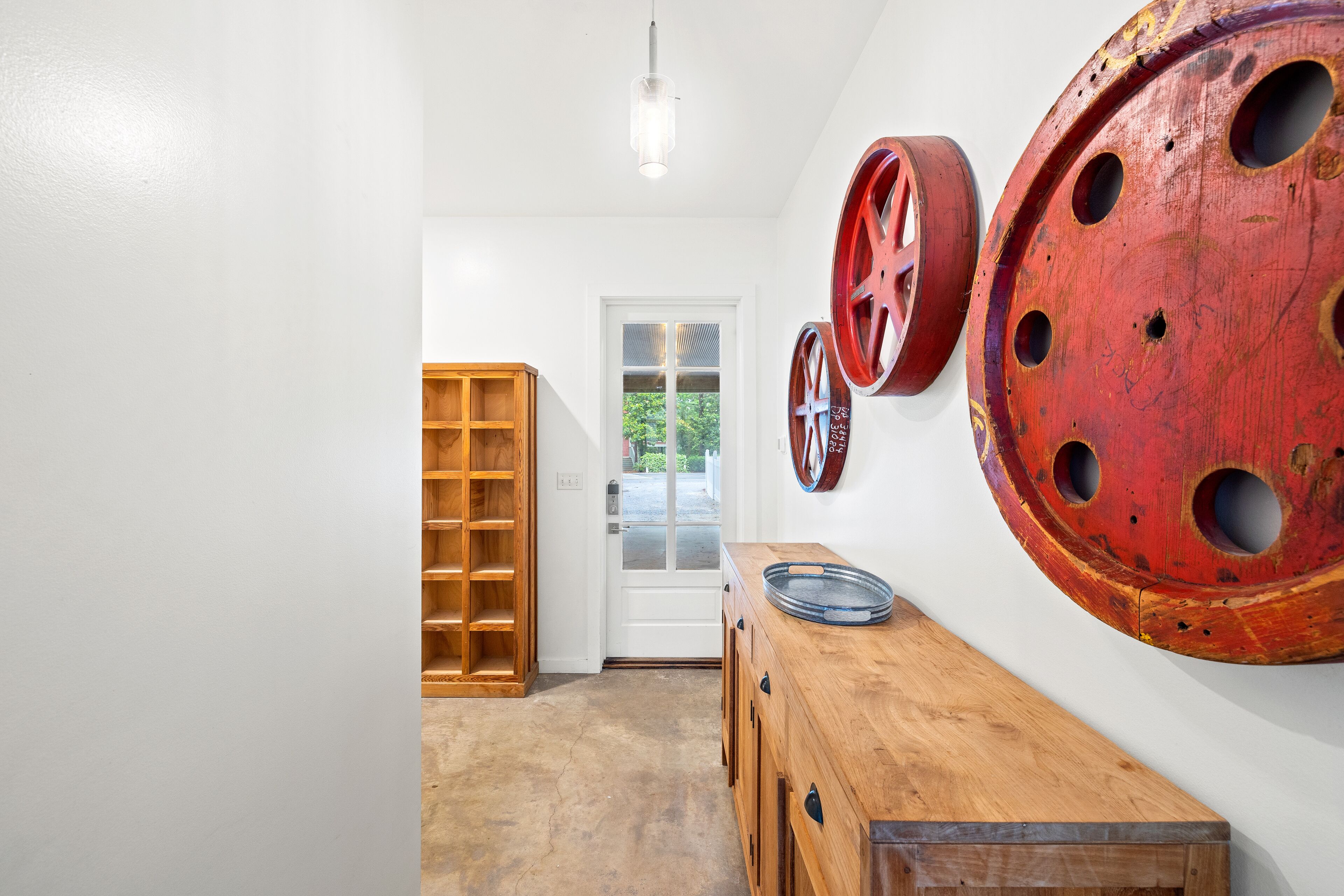 Un couloir avec un banc en bois, une étagère en bois et une grande décoration en forme de roue rouge accrochée au mur.
