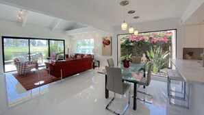 Un amplio salón con un sofá rojo, una mesa de comedor de cristal y vistas a un jardín a través de grandes ventanales.