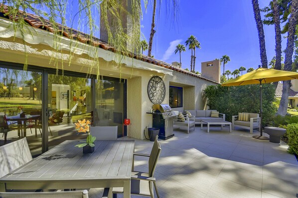An outdoor patio with a dining table, chairs, a grill, and a yellow umbrella.