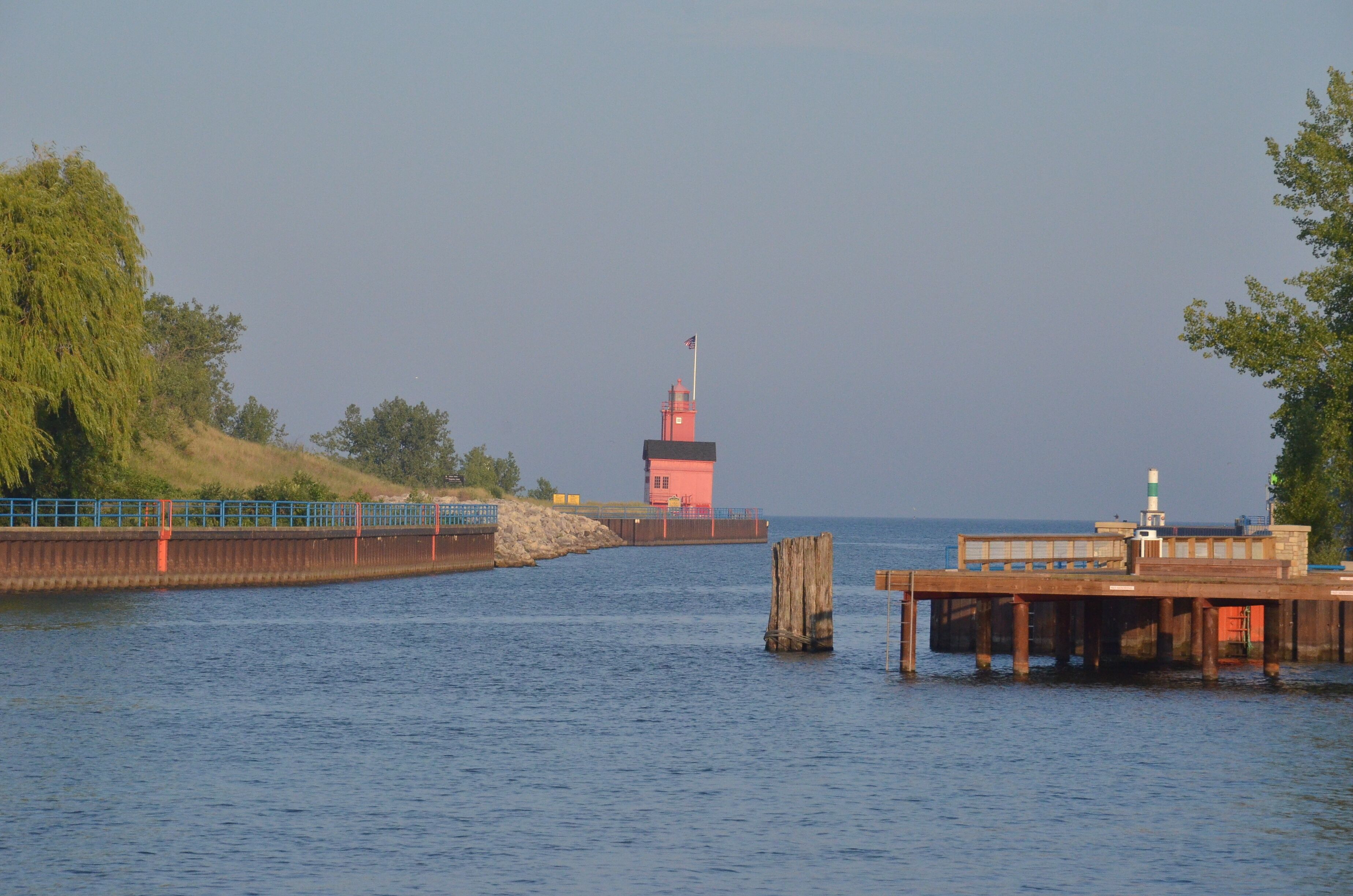 A waterfront scene with a red lighthouse, a wooden pier, and a blue bridge.