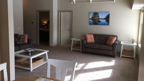 A living room with a couch, a coffee table, and a chair. There is a painting on the wall and a small table with a decorative item. - The Staterooms 2J, Directions, Newly Built, Seasonally Heated Pool, Beach Nearby (Holland)