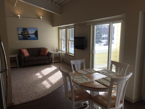 Uma área de refeições com uma mesa posta para quatro pessoas, um sofá, uma televisão e uma janela com vista para uma paisagem nevada.