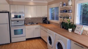 Une cuisine moderne dotée d’appareils électroménagers intégrés, d’un plan de travail en bois et d’une fenêtre avec des stores.