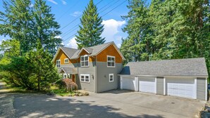 Une maison à deux étages avec un garage, entourée d’arbres.
