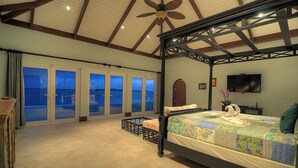 A spacious bedroom with a large bed, a ceiling fan, and a view through the glass doors. - Location!!! no car needed, Luxury Oceanfront, Our home on HGTV (Nassau)