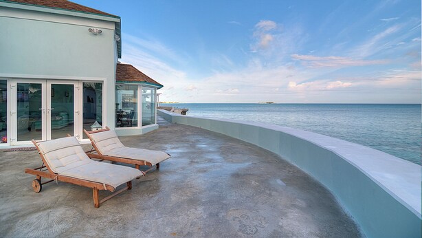 A balcony with two lounge chairs, a glass door leading to a room, and a view of the ocean. - Location!!! no car needed, Luxury Oceanfront, Our home on HGTV (Nassau)
