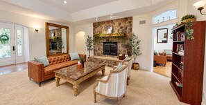 A spacious living room with a stone fireplace, leather sofa, and a bookshelf.