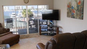 A living room with a TV, leather sofas, a glass table with a decorative item, and a balcony with a view of the marina. - DESTIN HARBORWALK, 3 bedrooms w/ Boatdock (destin)