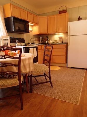 Una cocina con armarios de madera, microondas, refrigerador y una mesa de comedor con sillas.