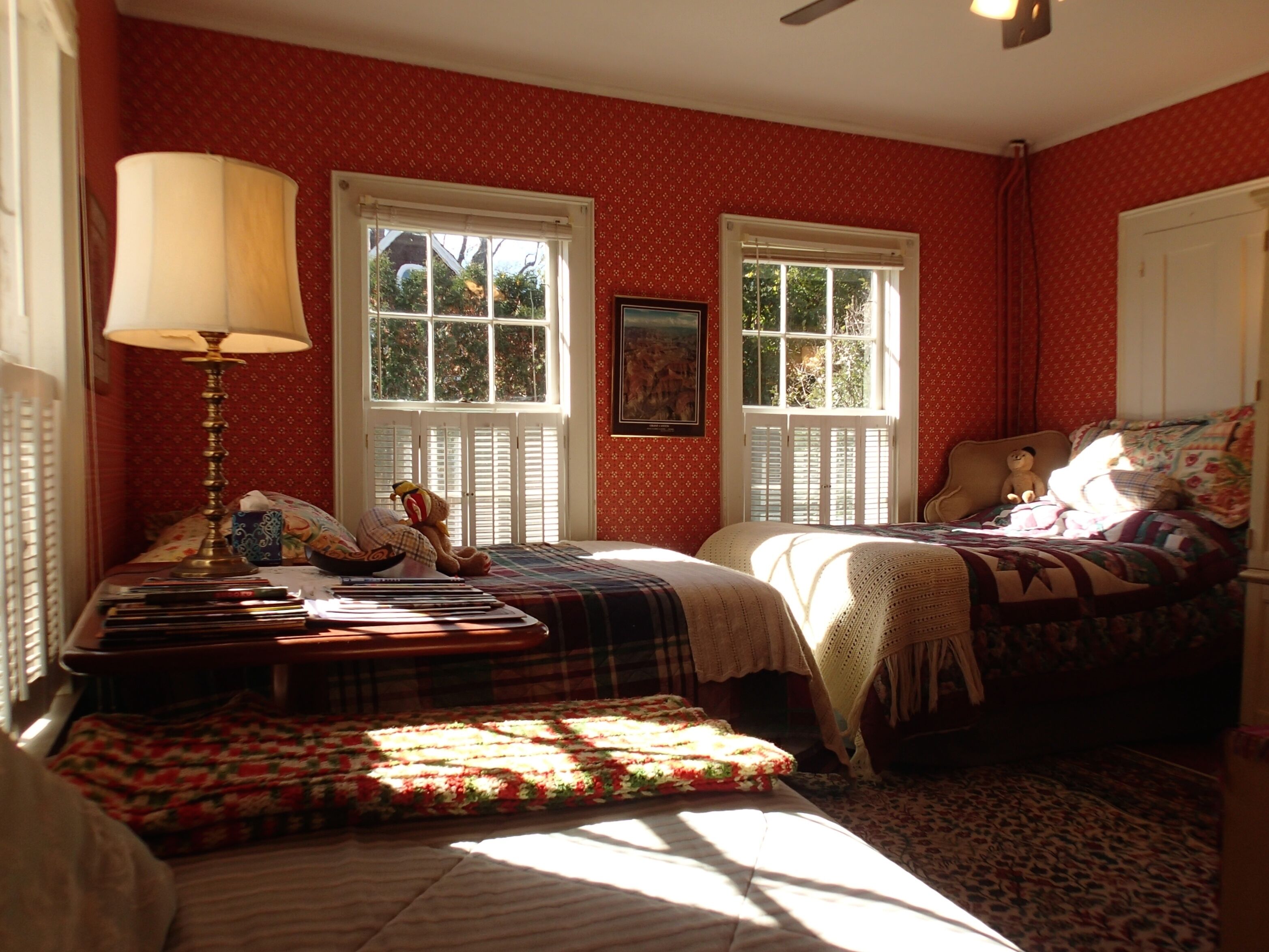 A bedroom with two beds, a nightstand, a lamp, and a window with shutters.