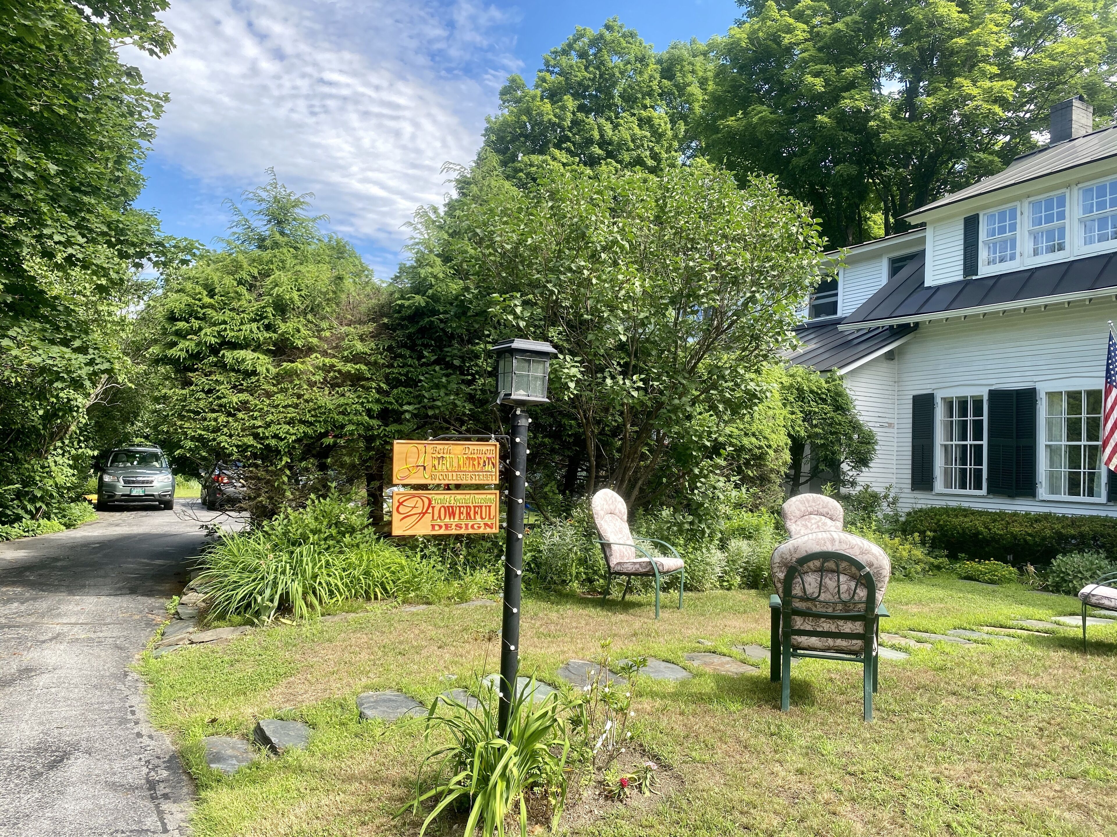A house with a sign for Beth Daniel's Flowerful Design, a lawn with chairs, and a stone pathway.