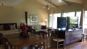 A spacious living area with a dining table, chairs, a sofa, a TV, and a ceiling fan.