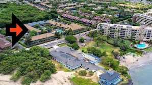 An aerial view of a coastal resort with beachfront properties, a large hotel, and a swimming pool.
